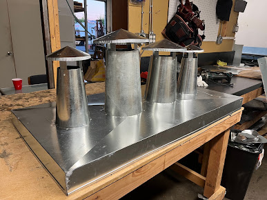 Metal assembly with multiple cylindrical outlets and caps on a workshop bench